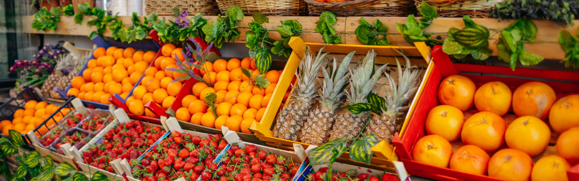 Bunte Obst-Auslage mit Erdbeeren, Orangen, Ananas und Wassermelonen vor einem Laden.